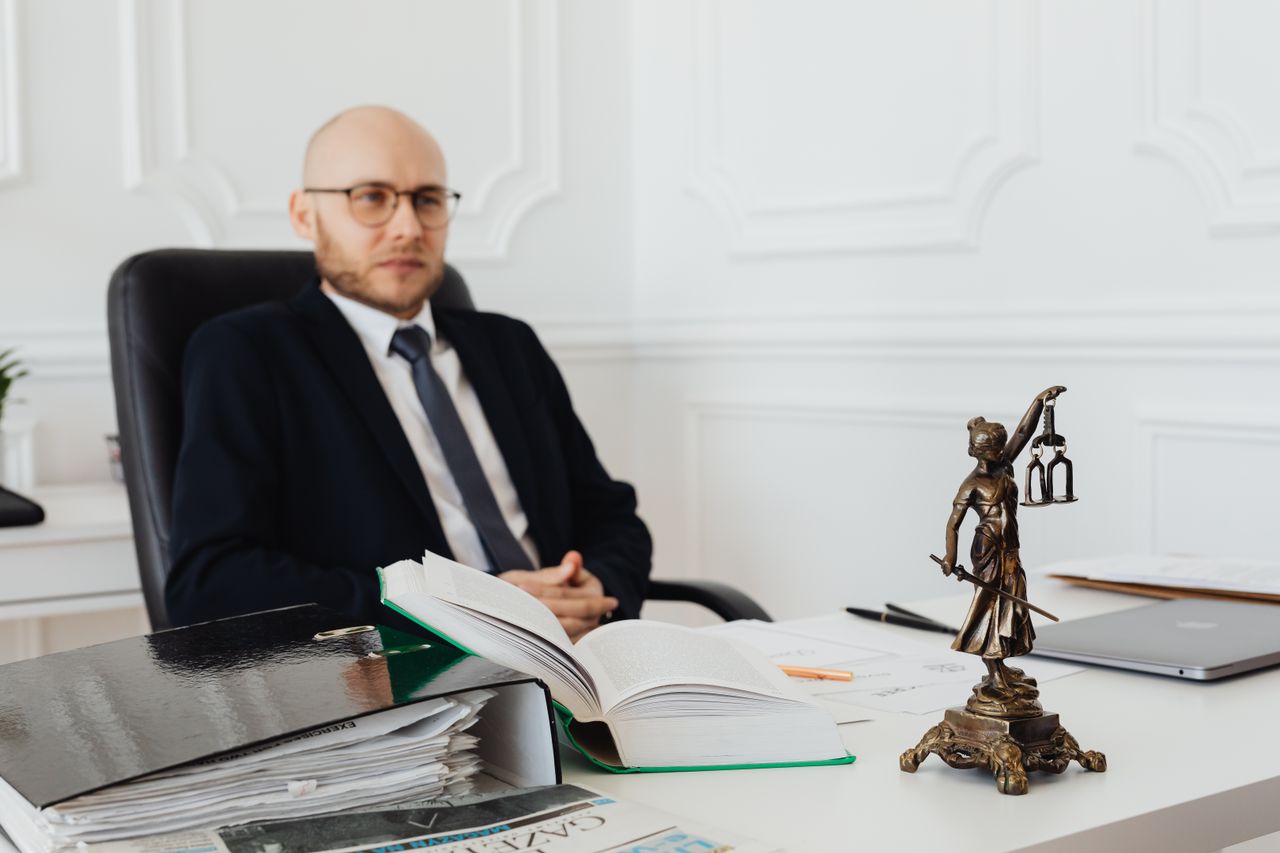 cta-bg Bald lawyer in office sitting with legal documents and Justice statue.